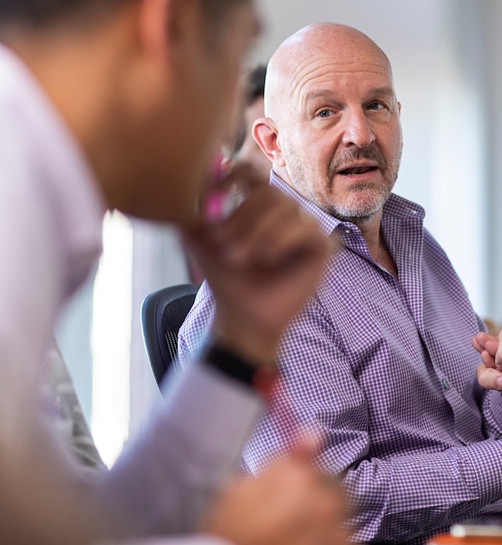 Totus team members around a conference room table with their attention focused on a data scientist who is enumerating some points.